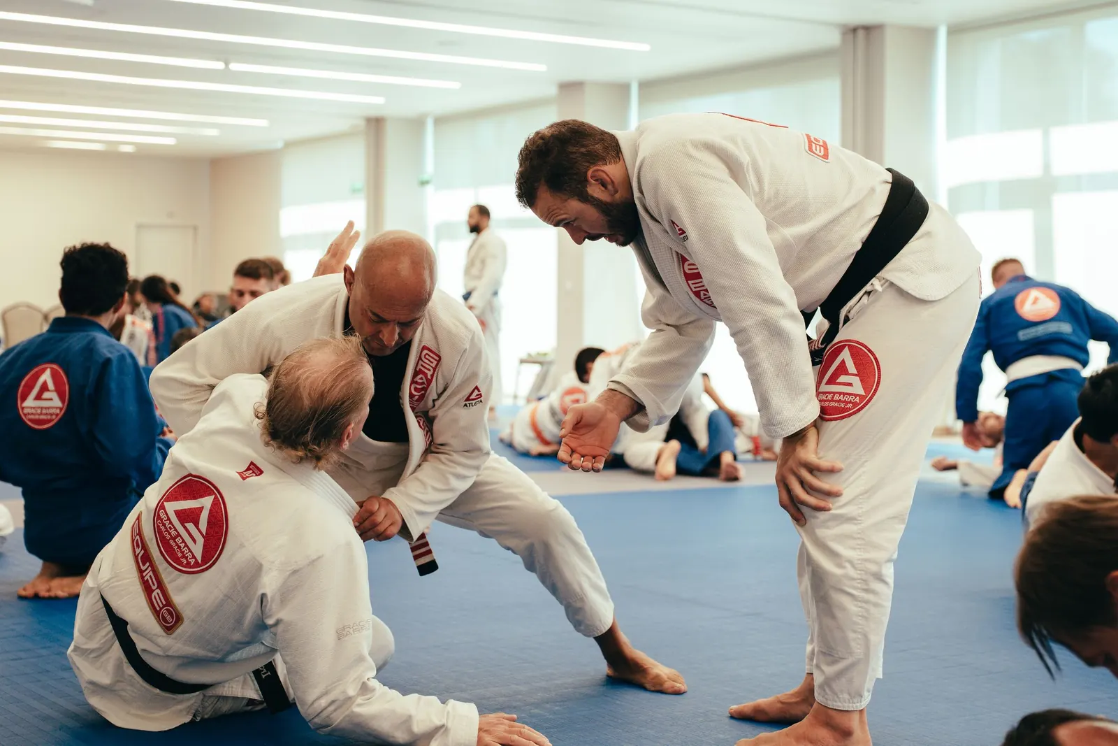 A black belt coach guiding two adult students through a drill on the mats
