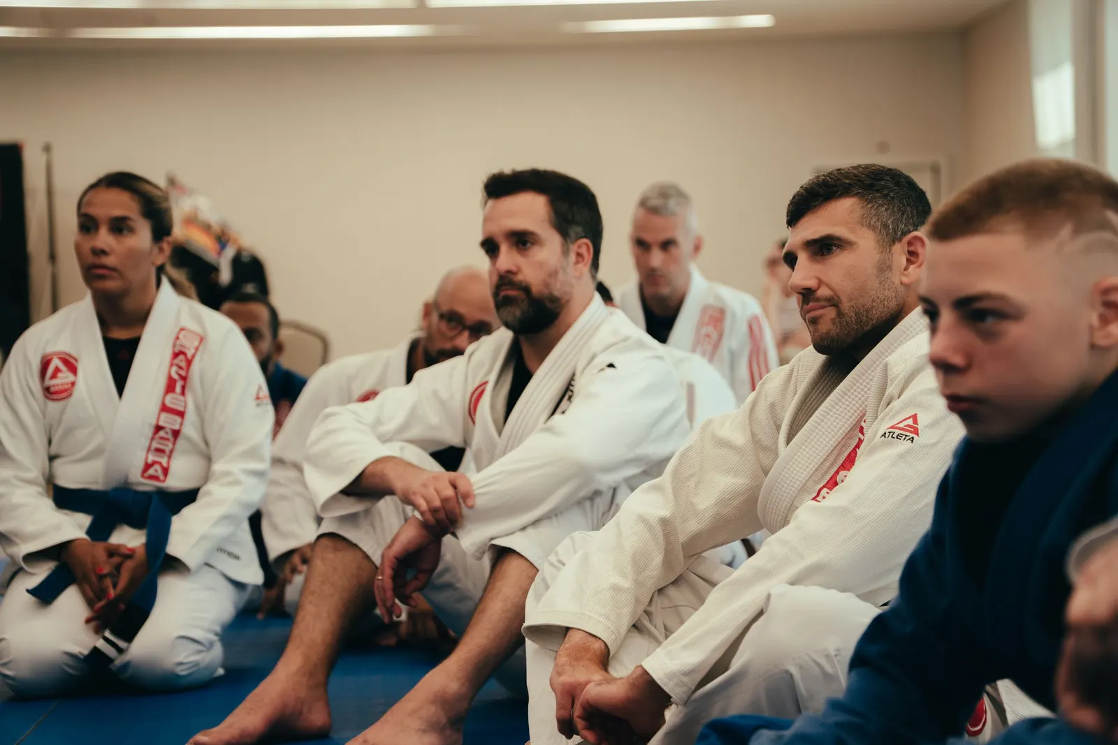 Adult students sitting on the mats and watching a coach