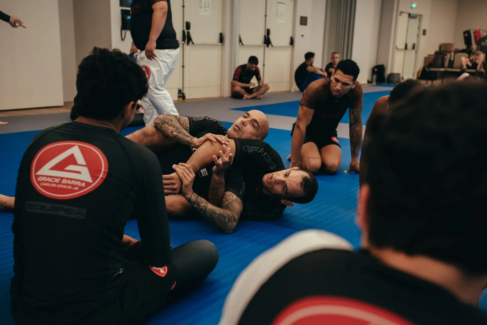 A coach demonstrating a no-gi submission while students watch