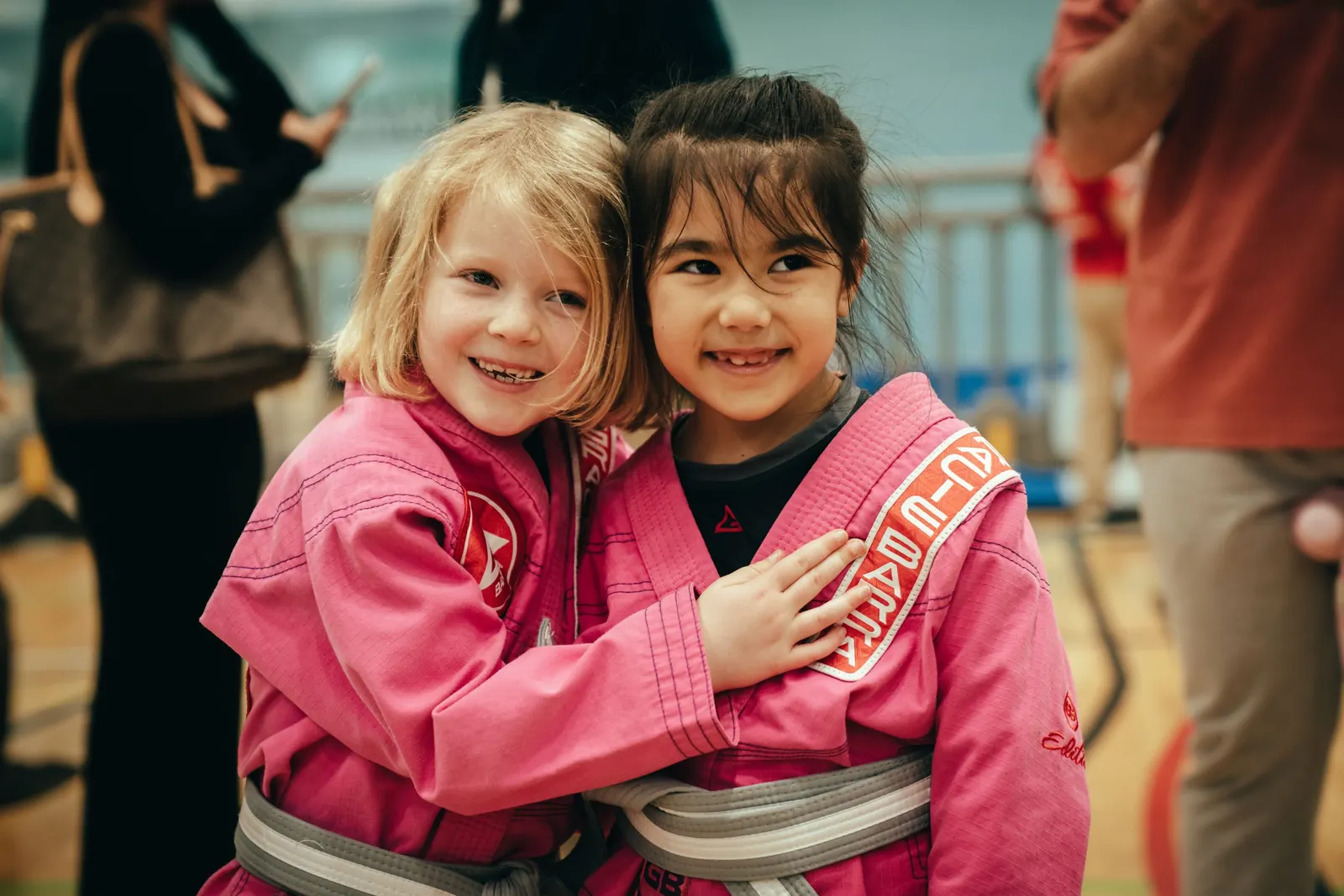 Two young students in pink gis smiling and hugging at a competition