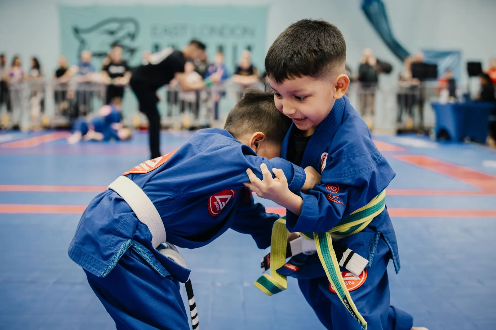 Two young students in blue gis grappling on a competition mat