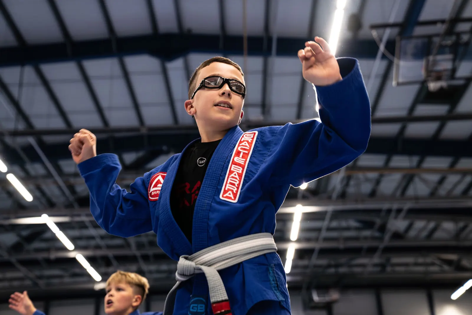 A young student in a blue gi raising both arms after a round