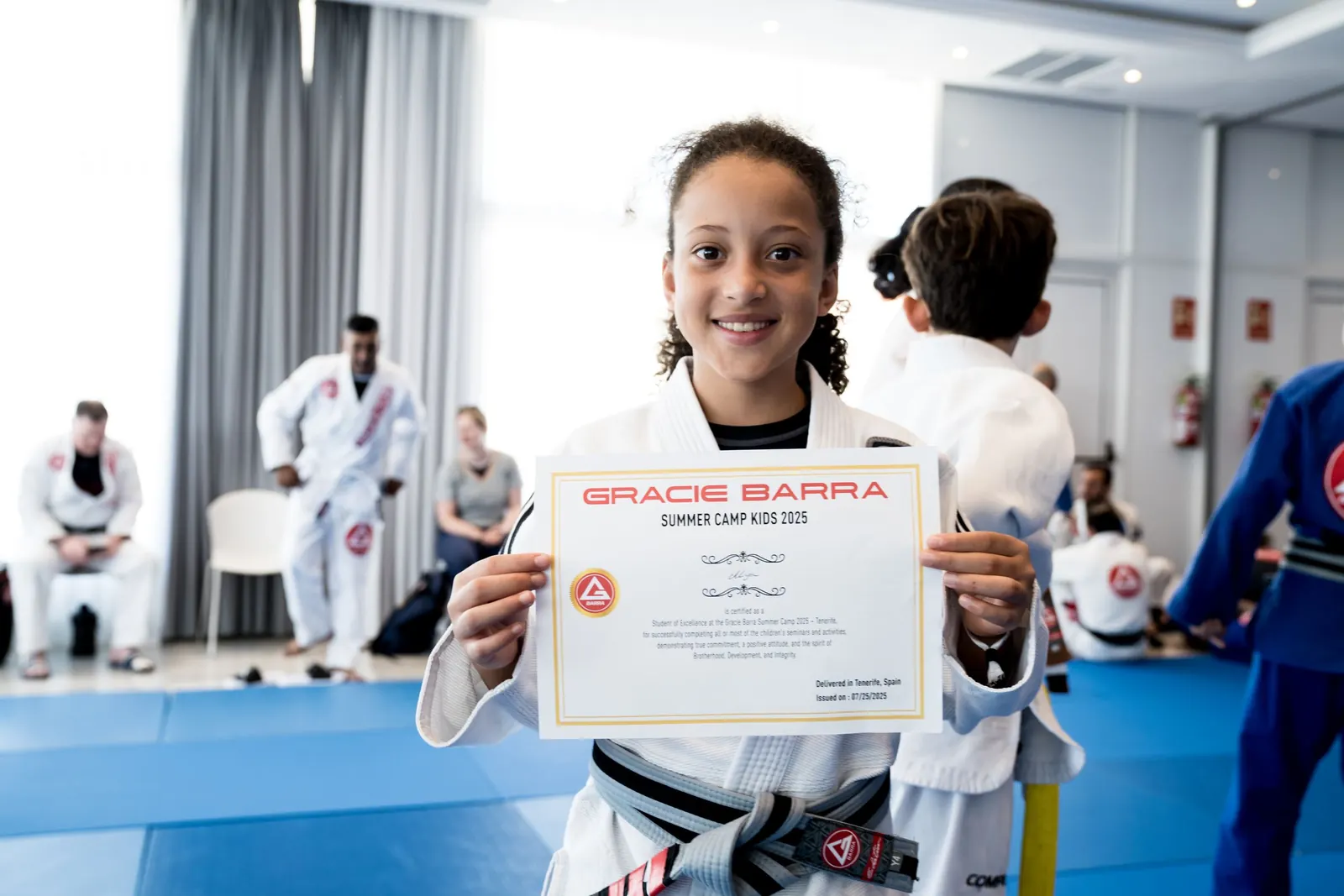 A young student holding a Gracie Barra summer camp certificate