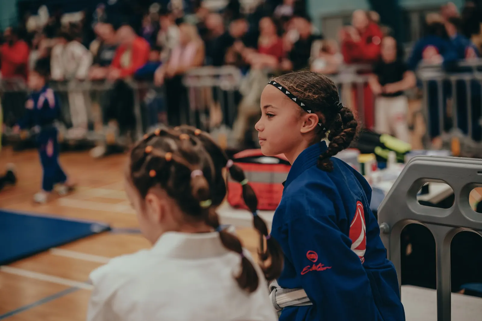 A young student in a blue gi sitting at the edge of the mat
