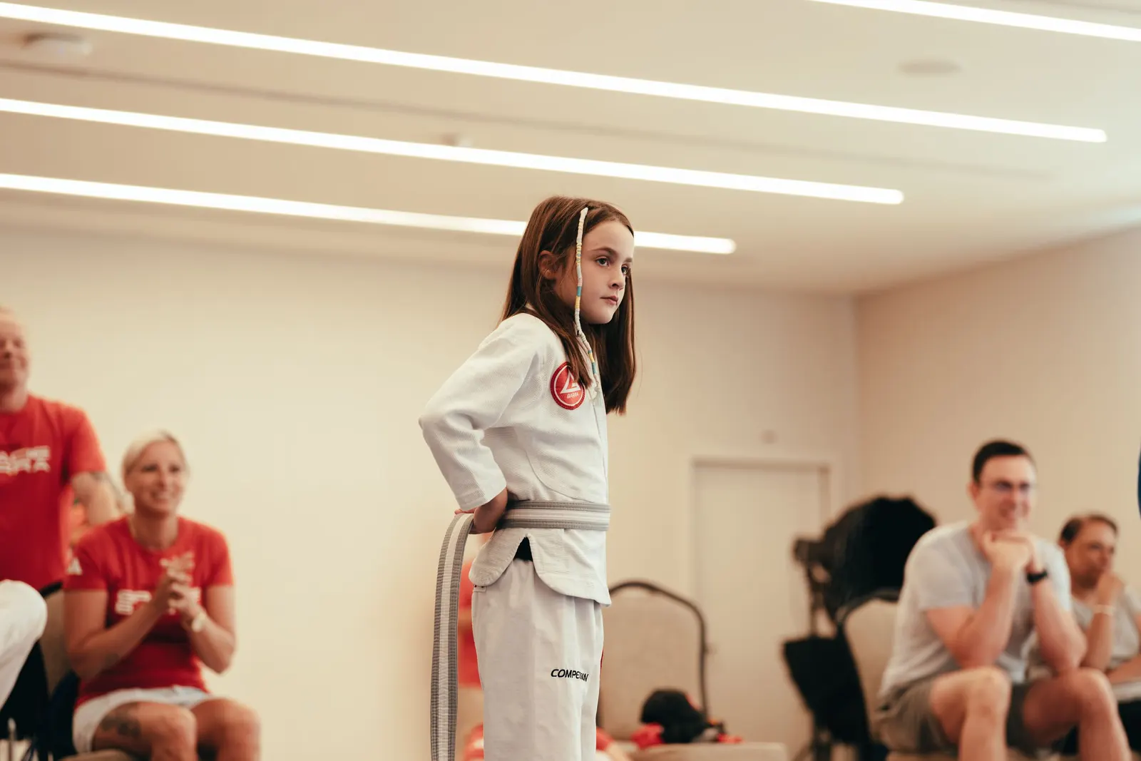 A young student in a white gi standing in front of a seated group
