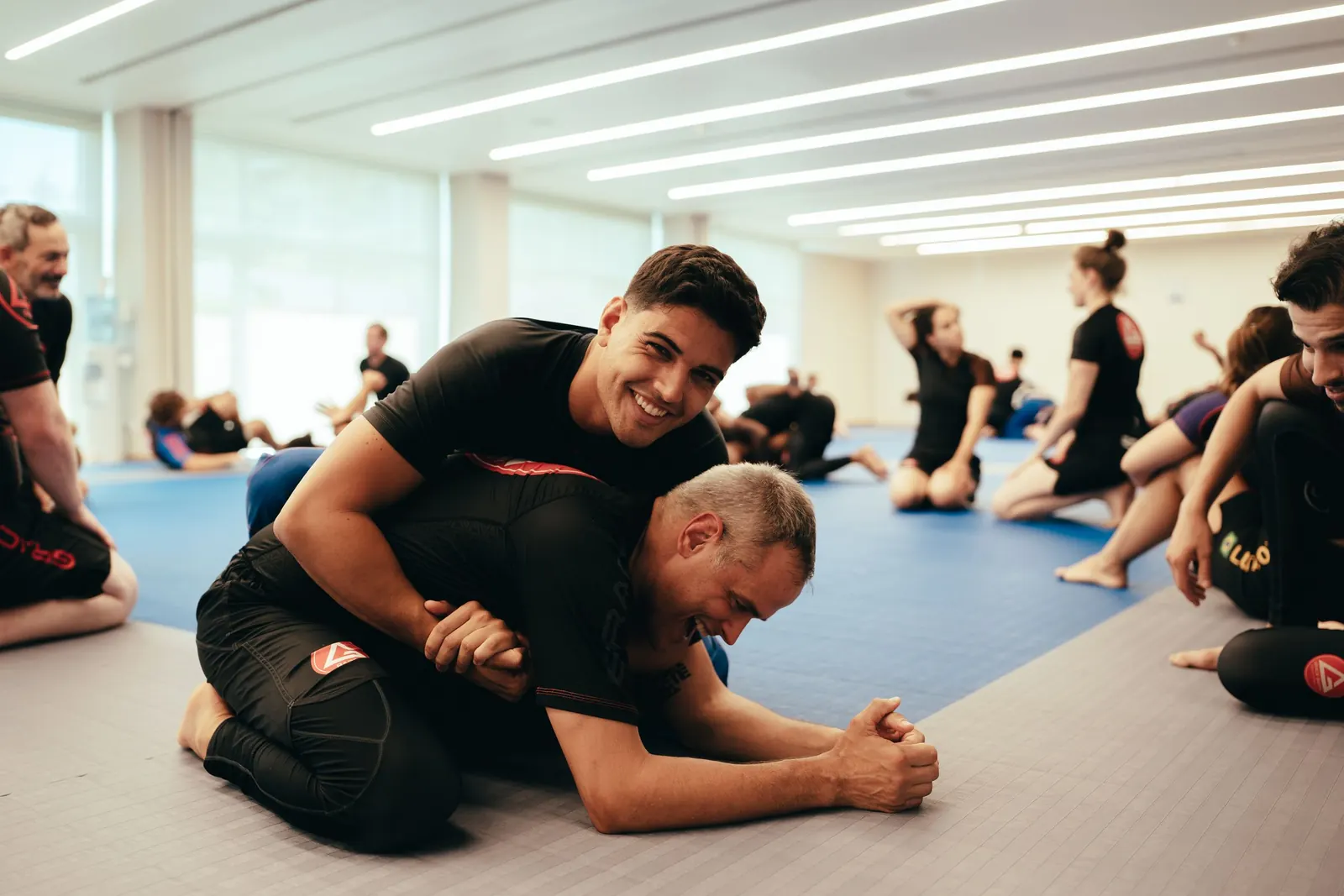 Two adult students smiling while practising a grappling position