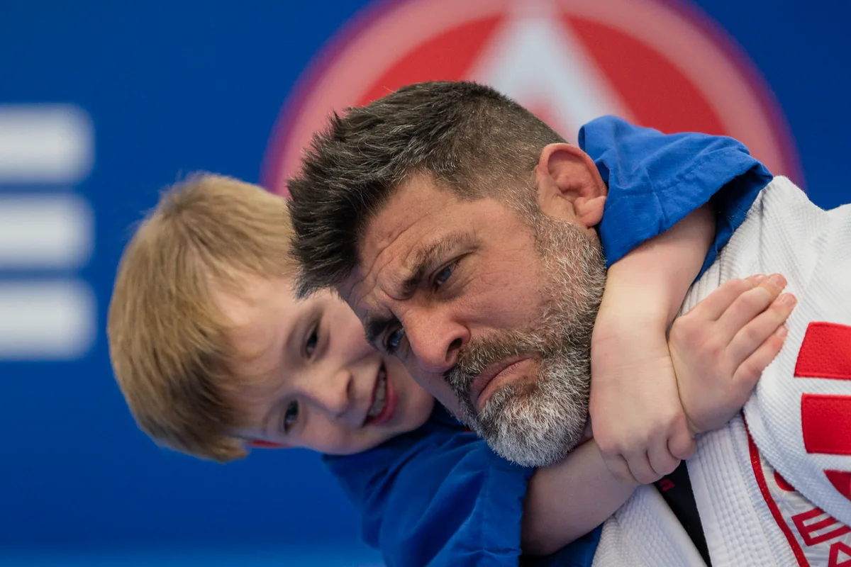 A child smiling while holding onto an adult during Jiu-Jitsu training